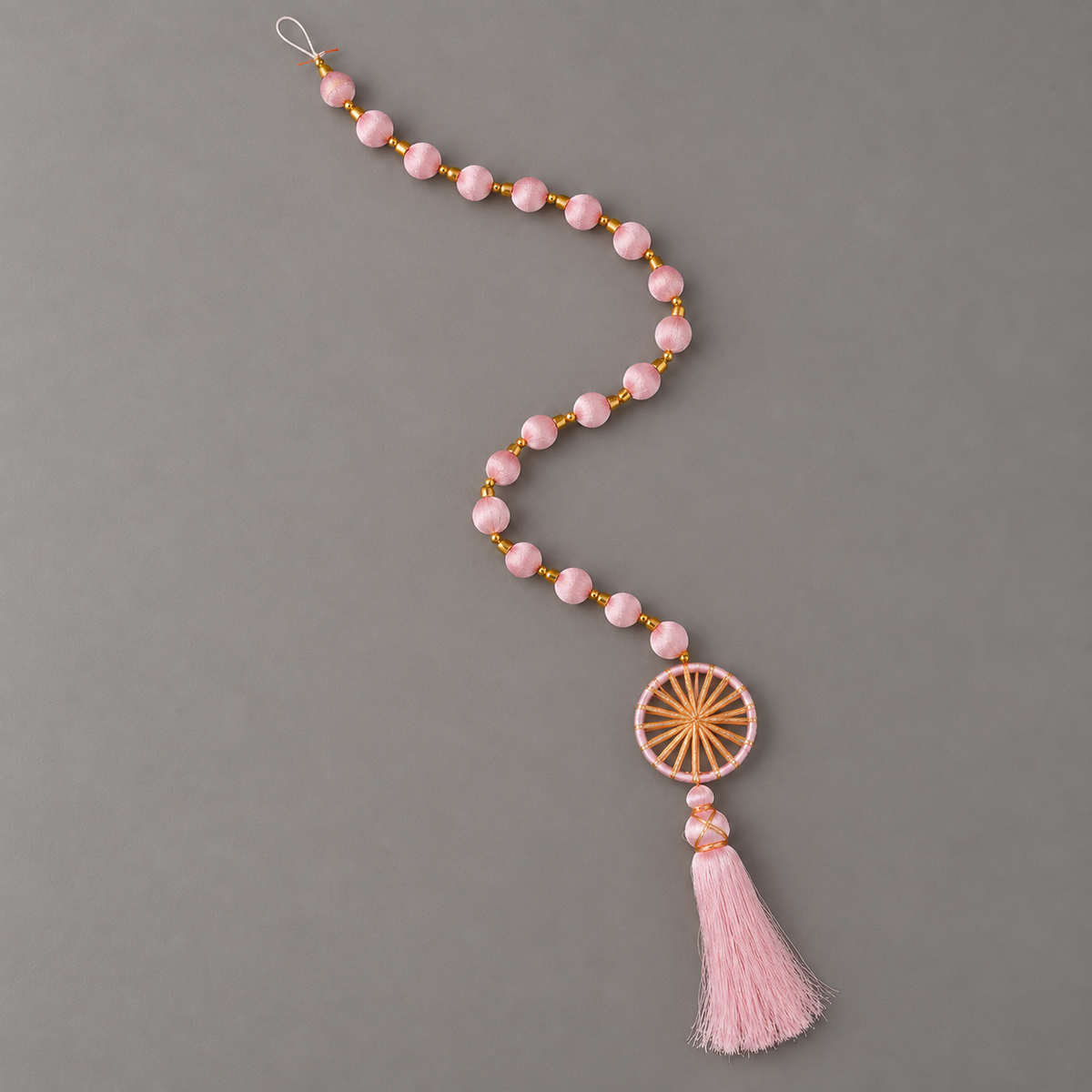 Full light pink sunburst ring and tassel hanging arranged in a curve on gray background